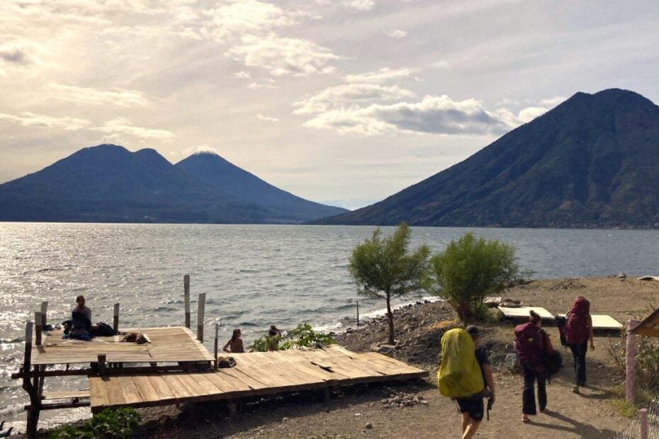 Backpackers walking on the shore of Lake Atitlan with volcanoes in the background