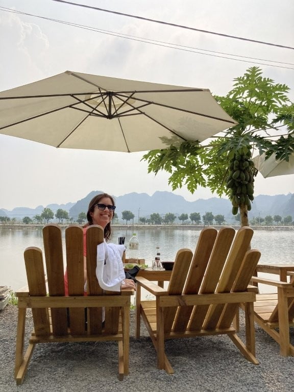 Woman sitting in lounge chairs under an umbrella overlooking rice fields in Tam Coc