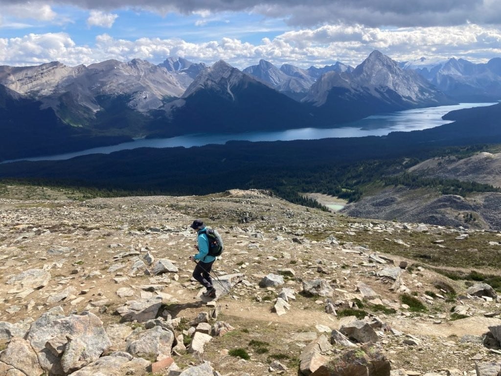 Man hiking on rocky slope overlooking Maligne Lake and sharp mountains