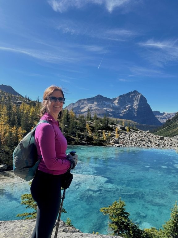 Woman in front of a clear blue lake and distant mountain peaks