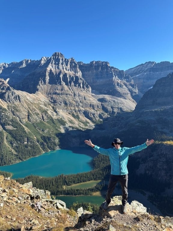 Man on a ridge trail with several lakes and mountain peaks in the distance