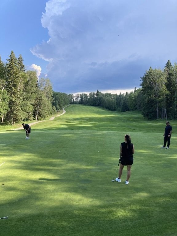 Golfers watching their playing partner putt with dark clouds in the distance