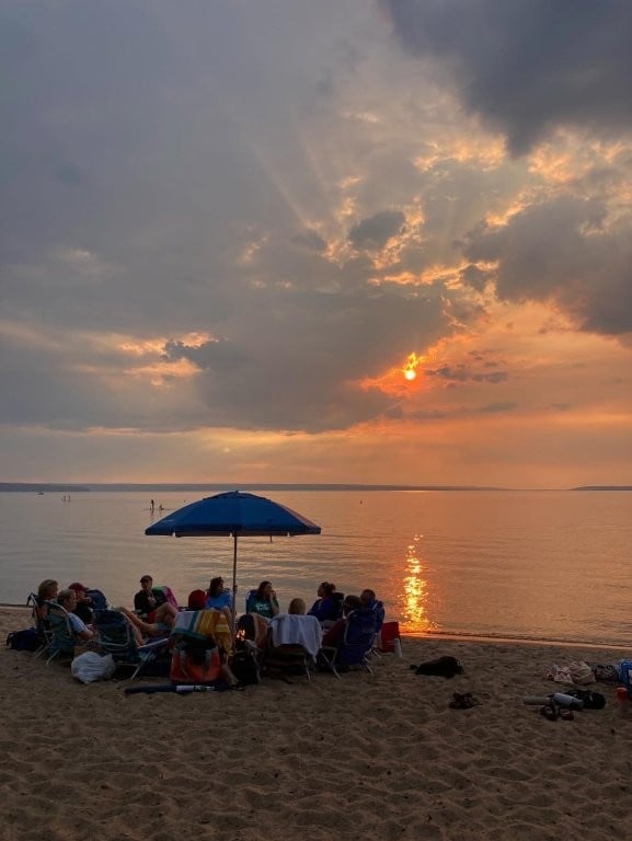Group gathered around a fire on the beach while the sun sets