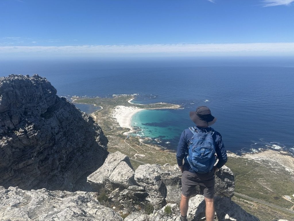 Man standing on rocky ledge overlooking beaches and ocean