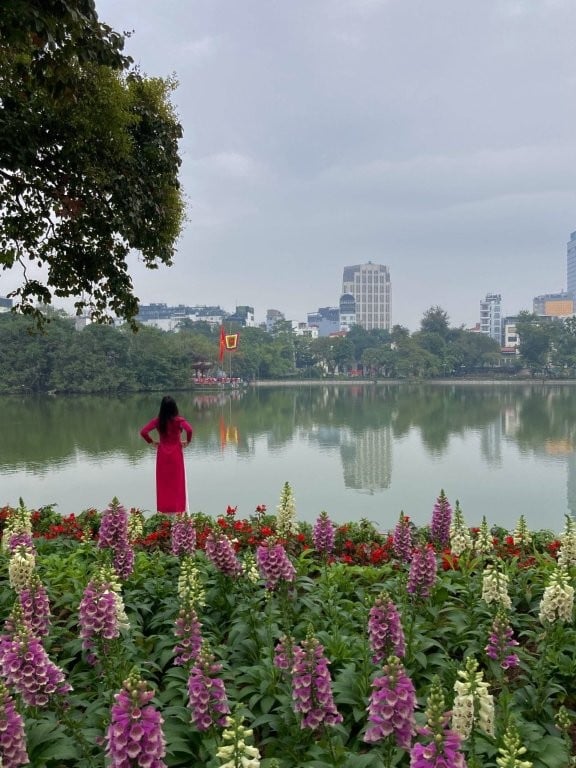 Woman in a red dress standing in front of flowers looking out over Hoan Kiem Lake in Hanoi Vietnam
