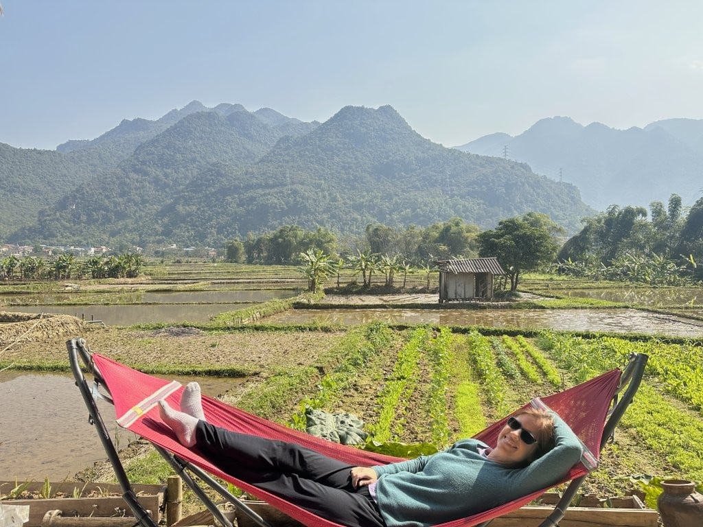 Woman in a hammock overlooking rice fields and hills to compare Ninh Binh vs Mai Chau