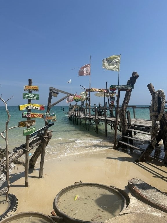 Signs and a rickety wooden dock on the shore in the Thai islands