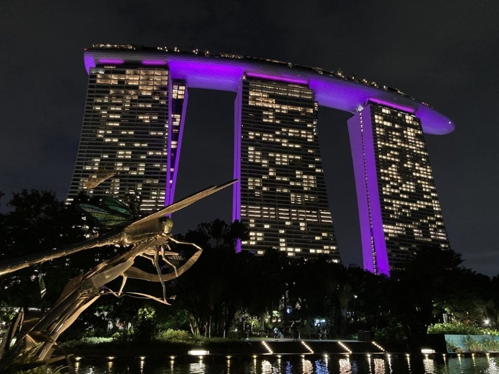 Three building hotel lit up in purple at night with a dragonfly statue in the foreground