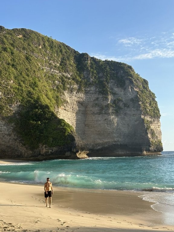 Man walking on Nusa Penida beach with cliffs behind