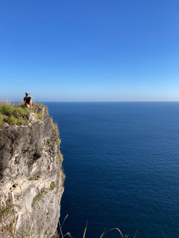 Woman sitting on cliff edge overlooking the ocean