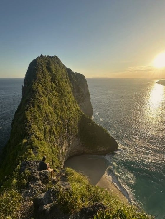 Man sitting on narrow ridge overlooking dramatic beach and cliffs
