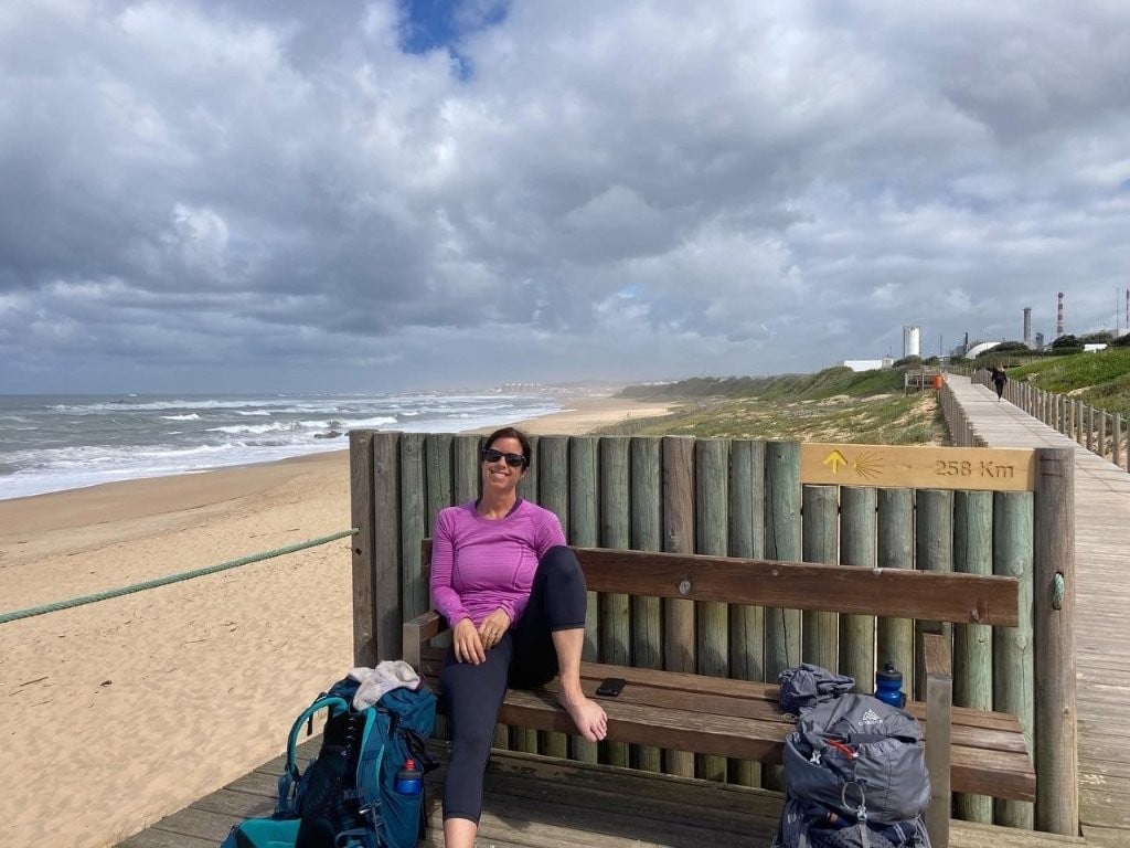 Woman with shoes off resting on boardwalk bench on the Camino Portuguese Coastal Route