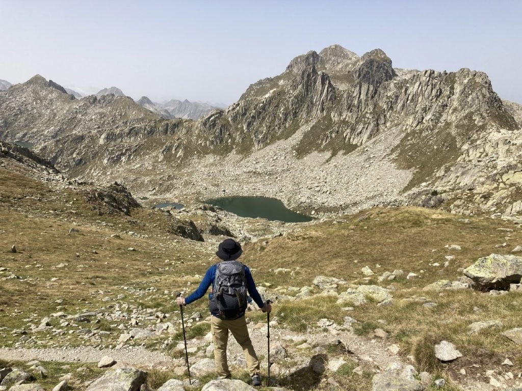 Hiker on trail overlooking rocky mountain lake and peaks