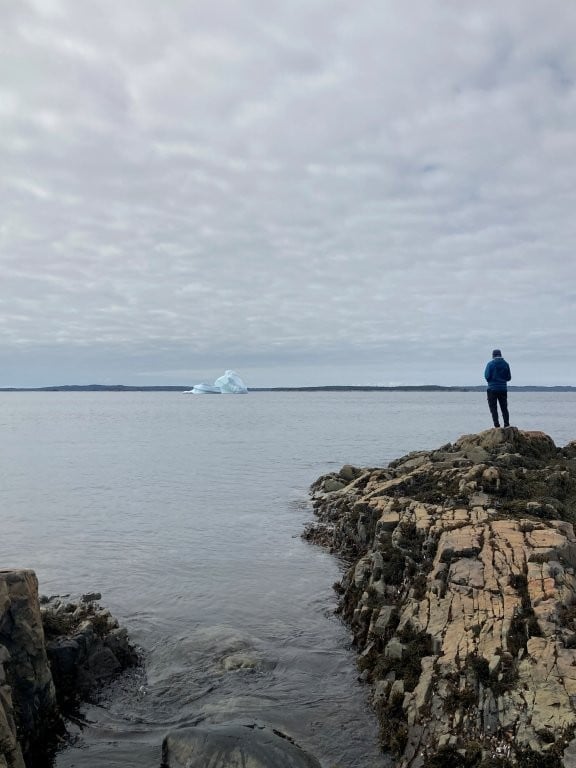 Man standing on rocky point looking out at distant iceberg