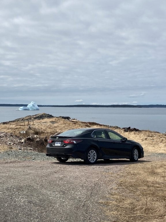 Black car parked with iceberg floating in the distance