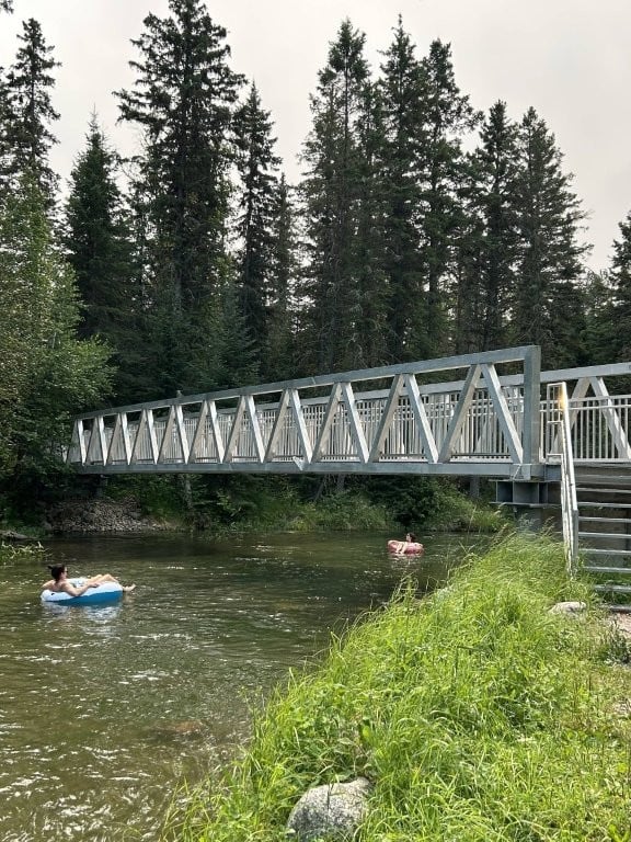People floating on a river underneath a metal bridge