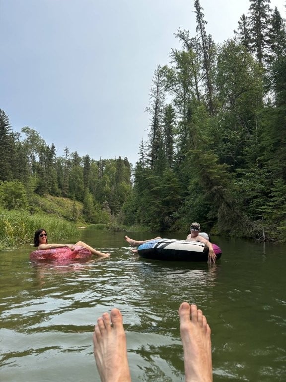 River floating with feet in foreground and two people in tubes in the background