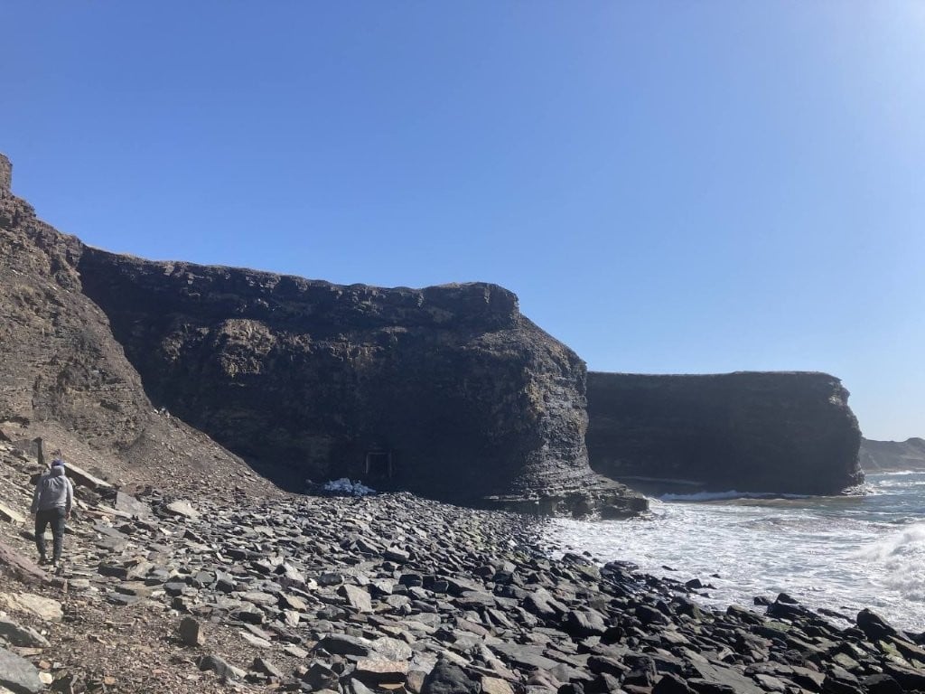 Hiker on rocky beach with cliffs behind