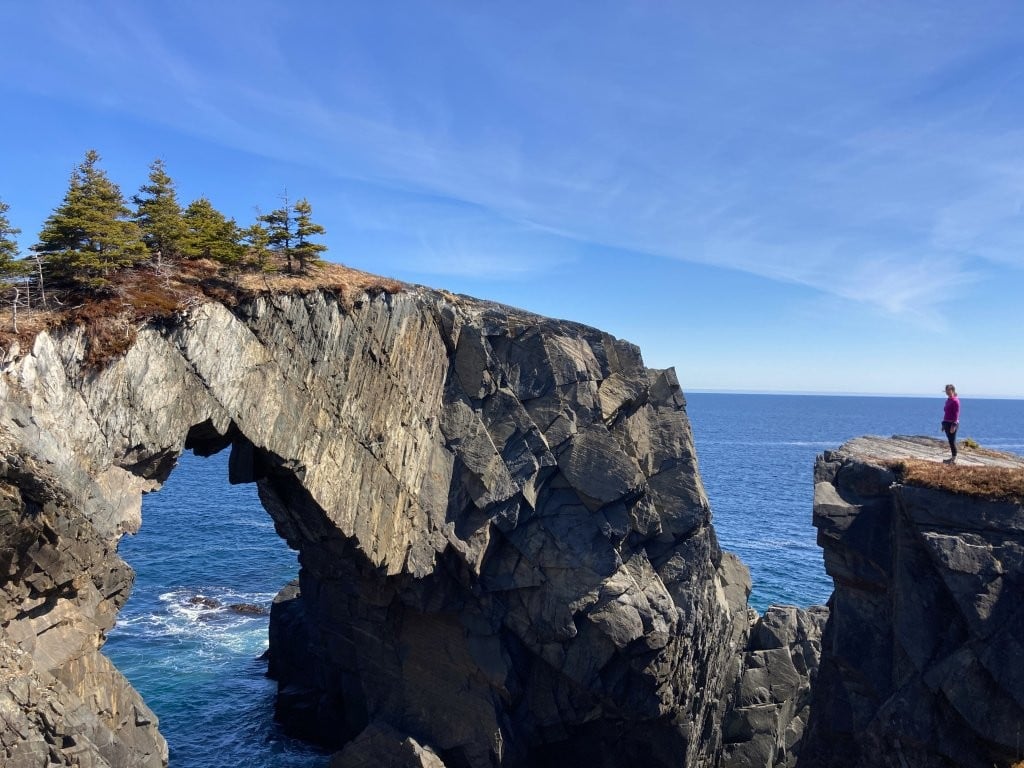 Woman on a rock looking at a large rock arch