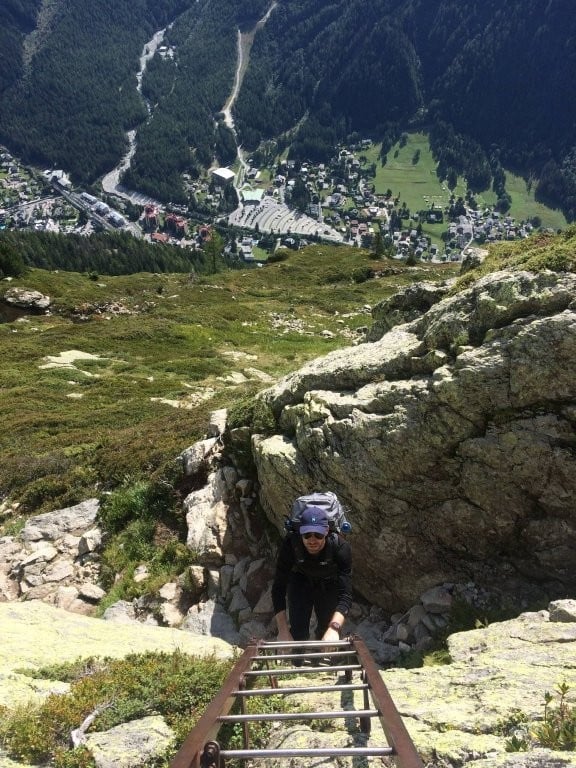 Man climbing a mountain ladder with village in valley far below