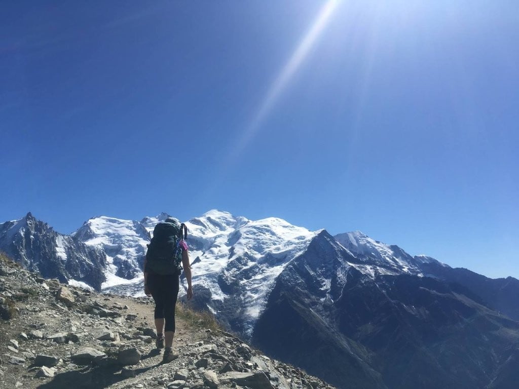 Hiker following rocky trail up toward snow-covered mountains