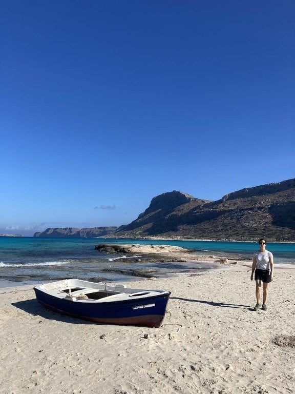 Woman walking on beach next to small fishing boat