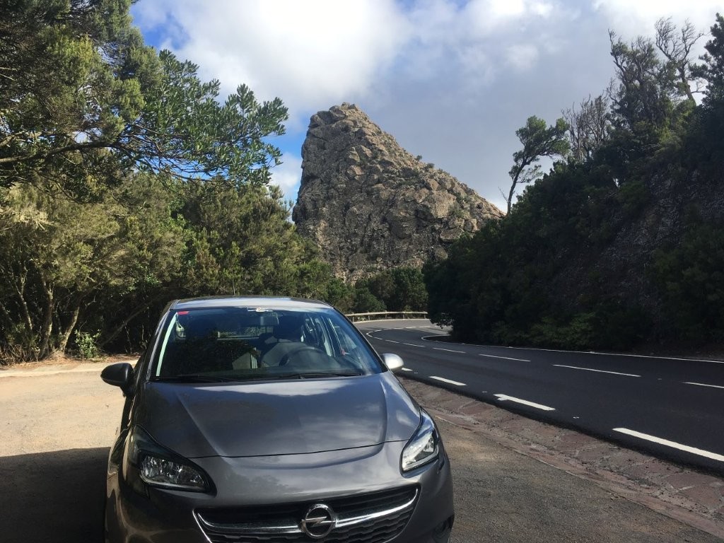 Car parked next to narrow highway with rocky hills behind