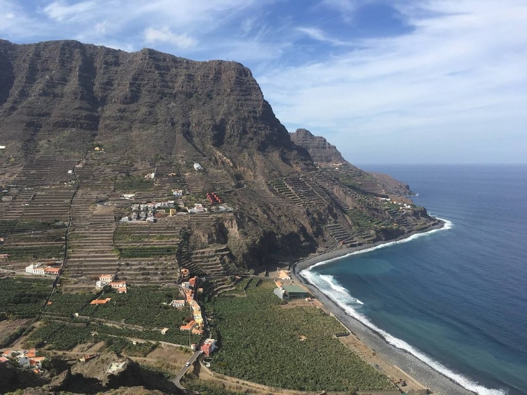 Tall cliffs overlooking green valley ending in black sand beach