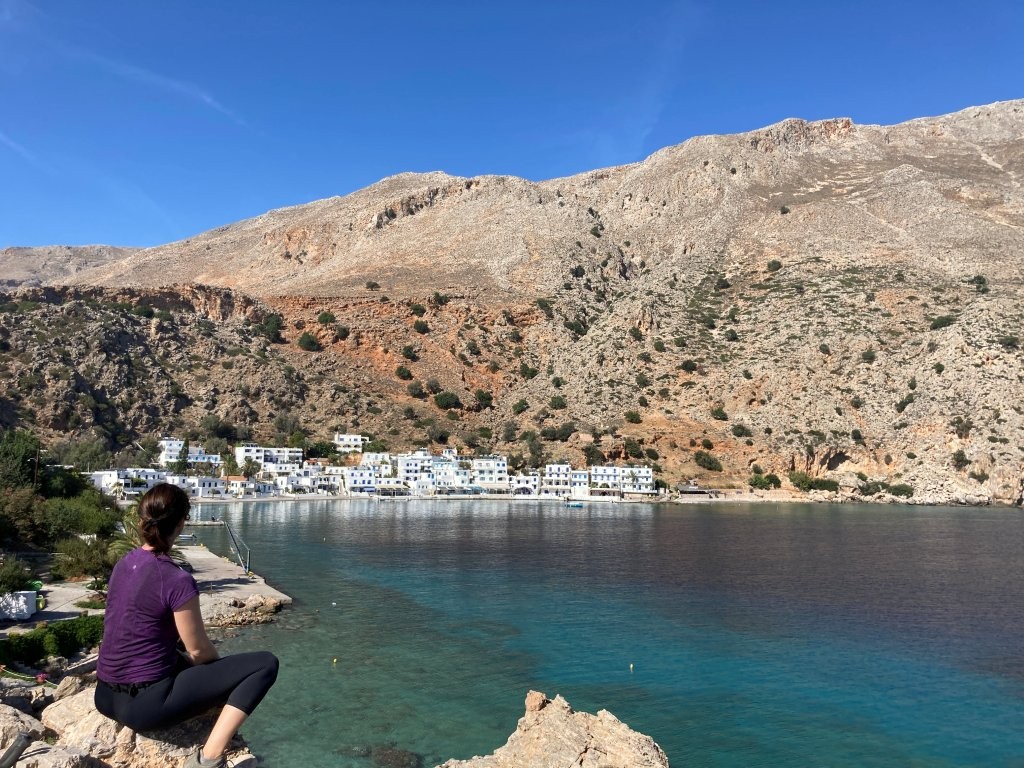 Woman sitting on rock overlooking calm bay and white village of Loutro