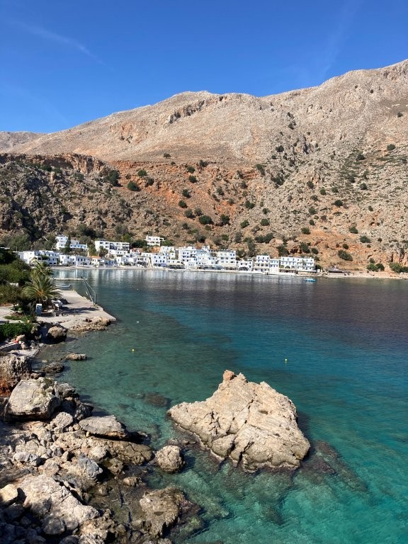 Clear water of bay with white village and rocky hills behind