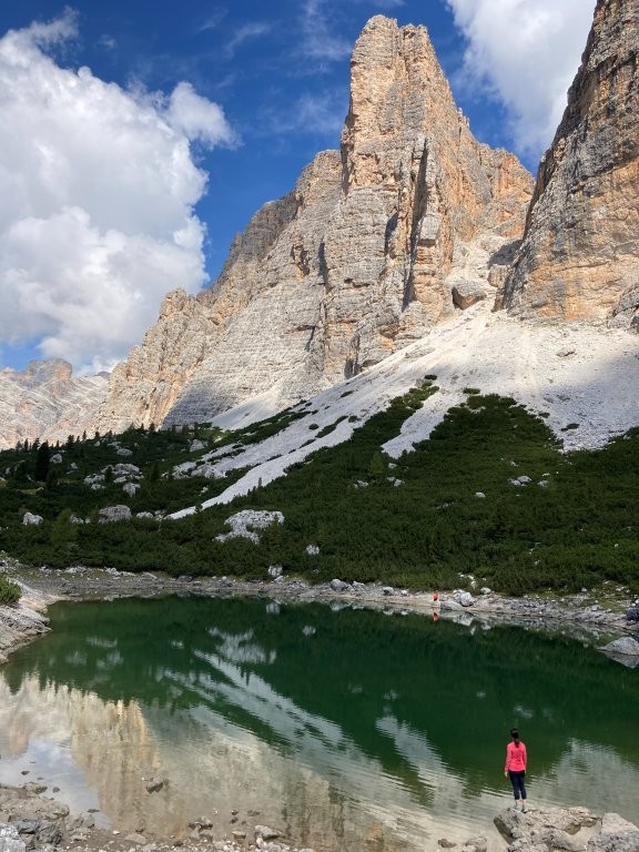 Woman standing on rock by alpine lake with tall mountains behind