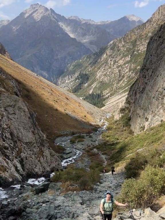 Woman hiking up steep valley with mountains behind