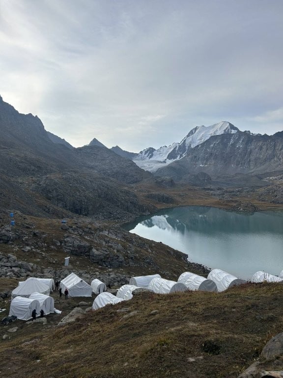 Collection of tents next to Ala Kul lake with glacier in background