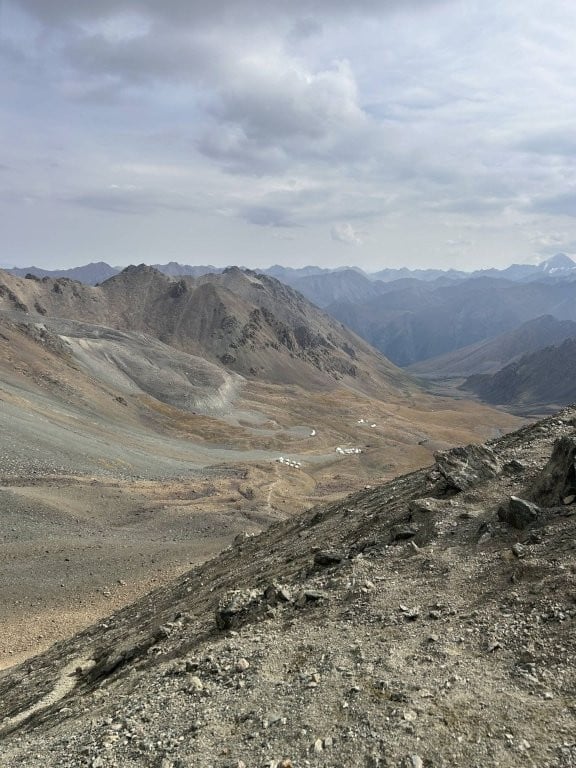 Steep rocky slope leading down to wide valley with yurt camps