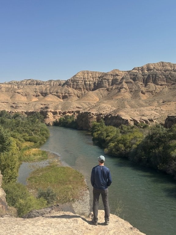 Man standing on rock overlooking river and badlands