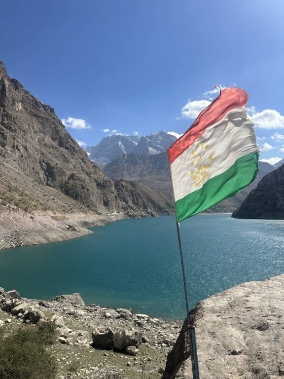 Tajikistan flag in front of a lake surrounded by mountains