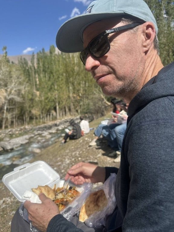 Man eating plov next to a small river