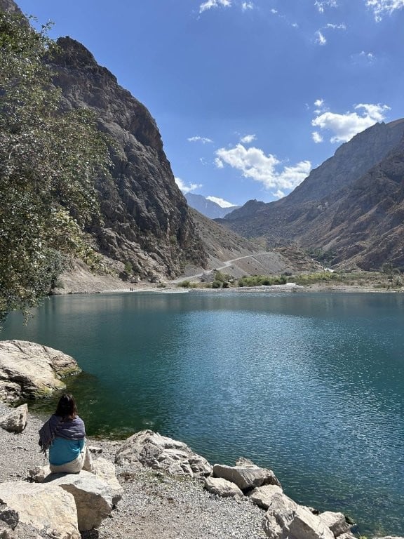 Woman sitting on a rock next to a calm alpine lake in Tajikistan